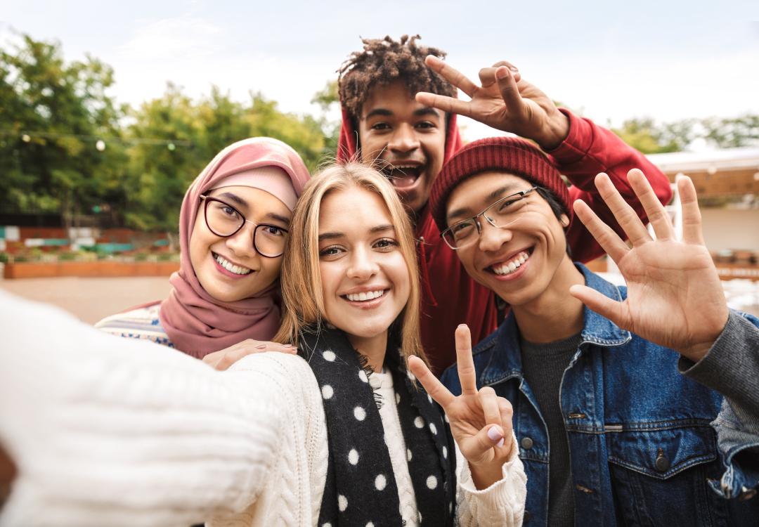 Vier verschiedene Jugendliche winken in die Kamera