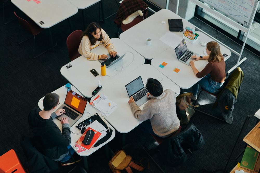 Mehrere Personen mit Notebooks sitzen an einem quadratischen Tisch