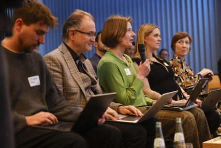 Personen sitzen in einer Reihe, eine Person spricht