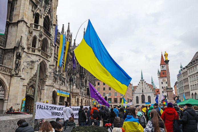 Zahlreiche Menschen haben sich eingefunden zur Ukraine-Kundgebung „Gemeinsam gegen den Krieg – ein Jahr des großen Krieges“ am 24. Februar 2023 auf dem Marienplatz. Eine große Ukraineflagge weht über der Menschenmenge. Zahlreiche Menschen haben sich eingefunden zur Ukraine-Kundgebung „Gemeinsam gegen den Krieg – ein Jahr des großen Krieges“ am 24. Februar 2023 auf dem Marienplatz. Eine große Ukraineflagge weht über der Menschenmenge.