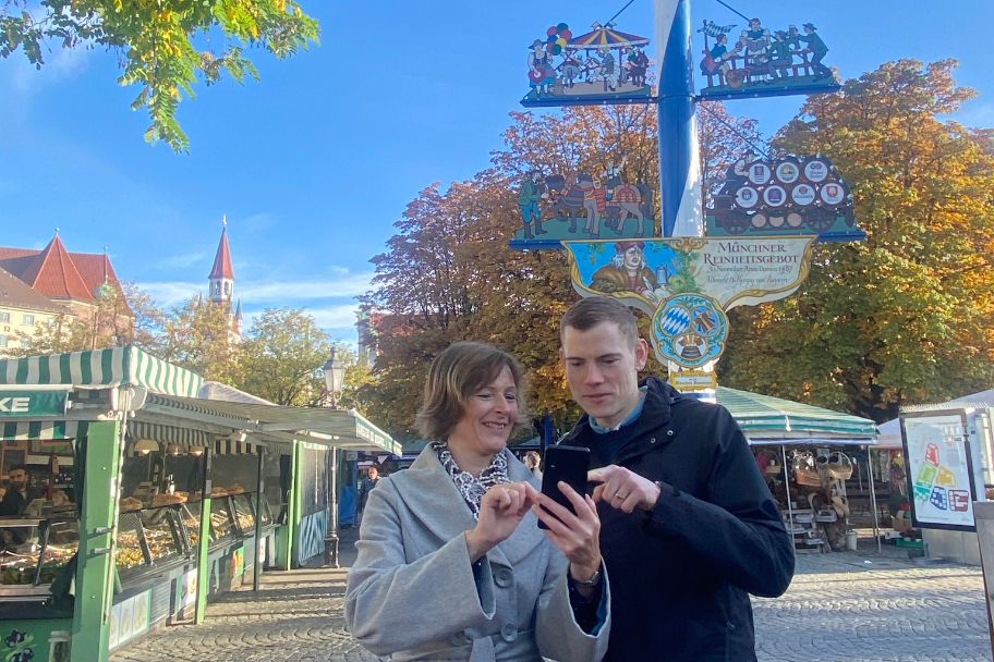 Frau und Mann mit Handy stehen vor dem Maibaum am Viktualienmarkt