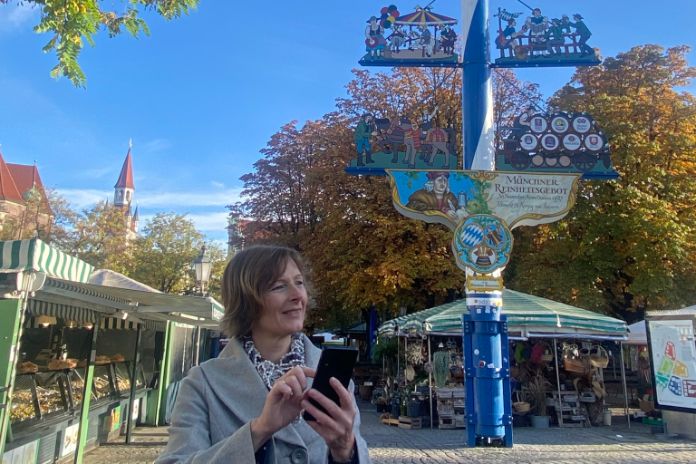 Stadterleben - Frau mit Handy vor dem Maibaum am Viktualienmarkt