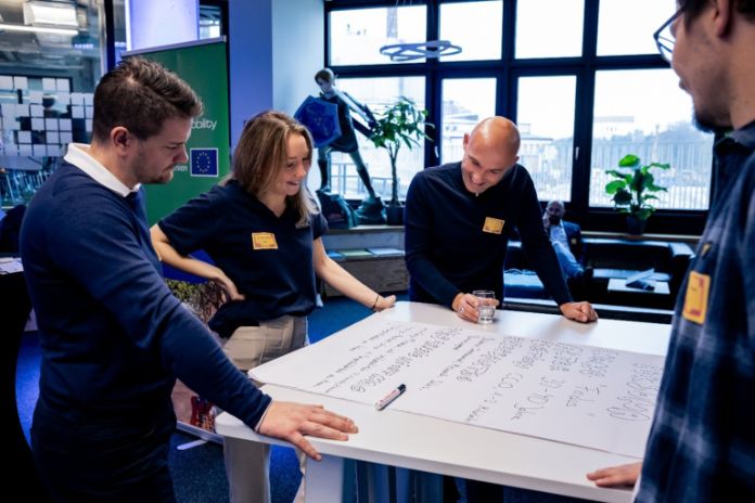 vier Personan schauen auf ein Papierplakat mit Notizen auf einem Tisch