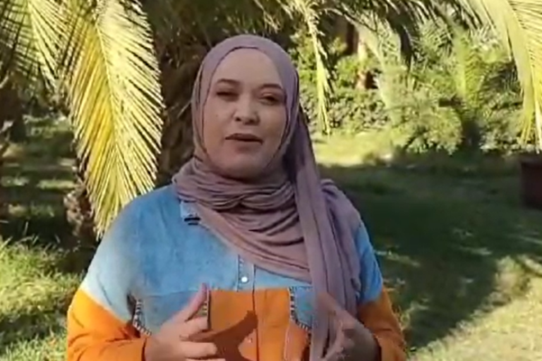 Eine Frau steht in Kasserine vor einer Palmenlandschaft und erklärt ihre Projektidee