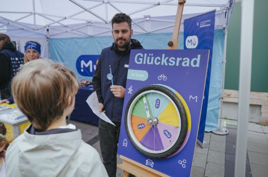 Mitarbeiter des Mobilitätsreferates und interessierter Junge vor einem Glücksrad