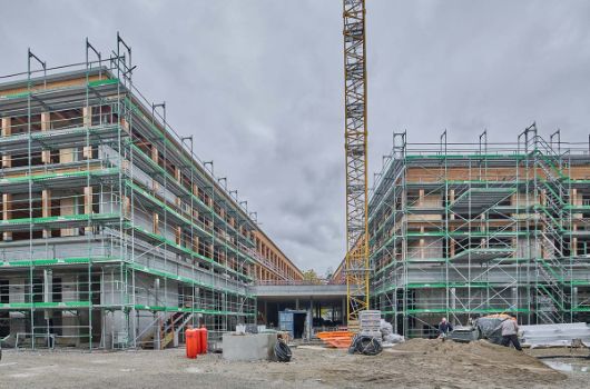 Blick vom zukünftigen Pausenhof auf die zwischen den Nord- und Südbaukörpern gelegene Pausenhalle, Handwerker mischen Estrich für die Einbringung in die Technikzentralen an