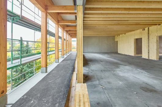 Blick auf den Aufbau der Brettsperrholzaußenwand, links davon: der in Stahlbetonbauweise errichtete Fluchtbalkon mit Holzstützen und -trägern, rechts davon: die Rippen der Holz-Beton-Verbunddecken und die Brettsperrholzflurwand 