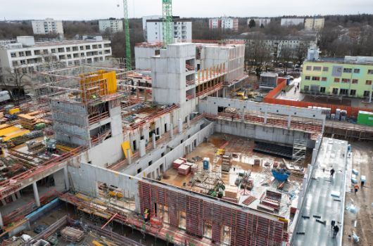 Luftbild mit Ansicht auf Holzgeschosse des Hauses für Kinder, die Rohbauten der Grundschule, des Verbindungsgebäudes, der Mittelschule sowie der Sporthalle..