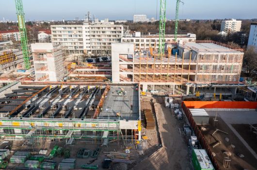 Luftbild-Ansicht der Holzbaugeschosse von Grundschule und Haus für Kinder sowie Dachbelegung der Sporthalle