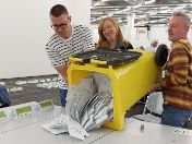 Drei Personen leeren eine Wahlurne auf einem Tisch aus.