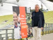 Auf dem Bild ist der Oberbürgermeister Dieter Reiter zu sehen. Er steht neben dem Kampagnenmotiv 