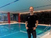 Das Foto zeigt den Kinder-Schwimmtrainer und Olympiamedaillen-Gewinner Christian Tröger vor einem Schwimmbecken im städtischen Versicherungskammer-Bad. 