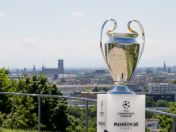 Champions-League-Pokal vor der Münchner Stadtsilhouette mit Blick über die Innenstadt.