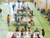 Blick von oben auf das Münchner Schulschachturnier mit zahlreichen Kindern an Schachbrettern in einer Turnhalle.