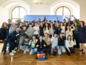 Große Gruppe von Jugendlichen und Erwachsenen posiert jubelnd bei der Schulsportehrung vor einer blauen Fotowand mit München-Logo. Einige tragen Medaillen.