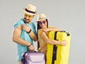 Junger Mann und junge Frau mit Sonnenhüten und Koffern