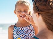 Mädchen wird von Frau im Gesicht mit Sonnenschutzcreme eingecremt