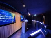 Raum mit gedimmtem Licht, Fernsehern an der Wand und Podien mit Tablets gegenüber