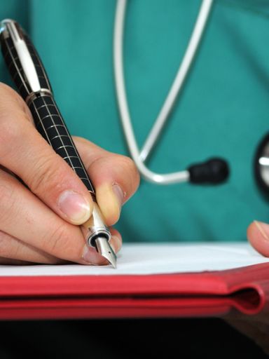 Ärtin mit Stethoskop schreibt etwas auf ein Blatt.
