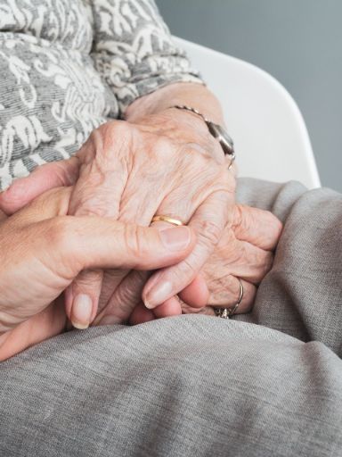 Eine junge Hand hält eine die Hand einer älteren sitzenden Dame