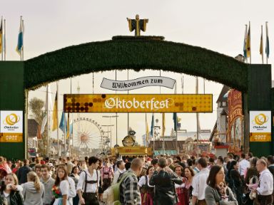 Eingang zum Oktoberfest mit Menschenmengen und Fahrgeschäften im Hintergrund